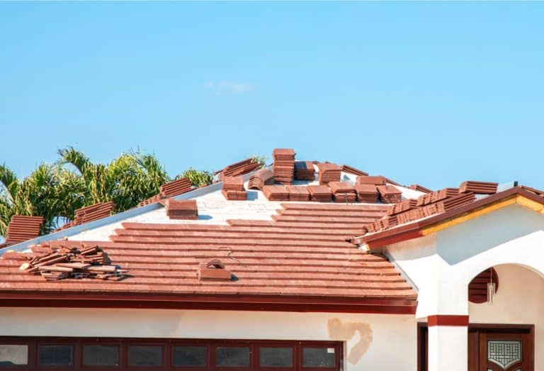 Red tile roof undergoing replacement with new roofing materials and stacked tiles on a residential home.
